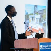 Scholar giving oral presentation, wearing mask.